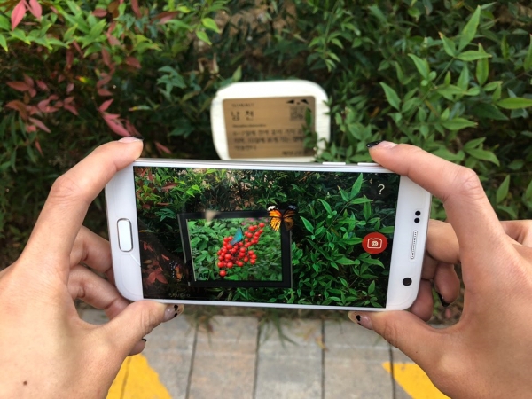 ‘반포 써밋 AR 가든’ 앱을 이용해 단지 내 식물 팻말에 적용된 열매 맺는 애니메이션을 보는 모습. (사진=대우건설 제공)
